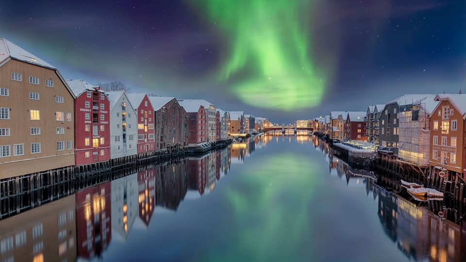 En kanal med byggnader på båda sidor. Norrsken på en mörkblå himmel.